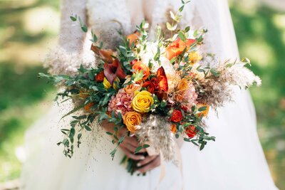 Bride holding red orange and yellow floral bouquet