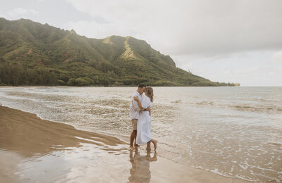 Couple on calm beach wearing white with green mountain behind