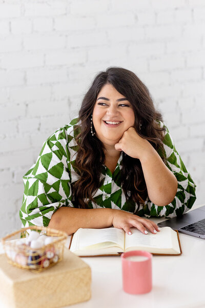Marissa Martinez in a green and white patterned dress sitting at a table with her Bible and smiling