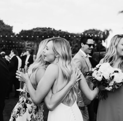 bride hugs wedding guest with cocktail in hand