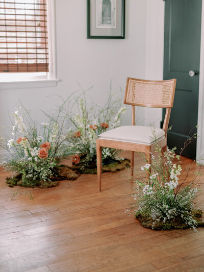A wicker chair is surrounded by three floral arrangements indoors.