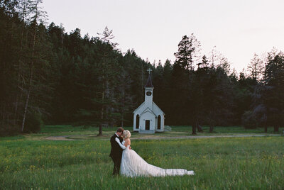 A Washington wedding photographer captures a twilight embrace by a meadow chapel, uniting love and nature.