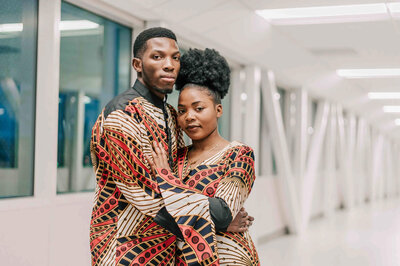 Husband stands behind wife with his arms around her.