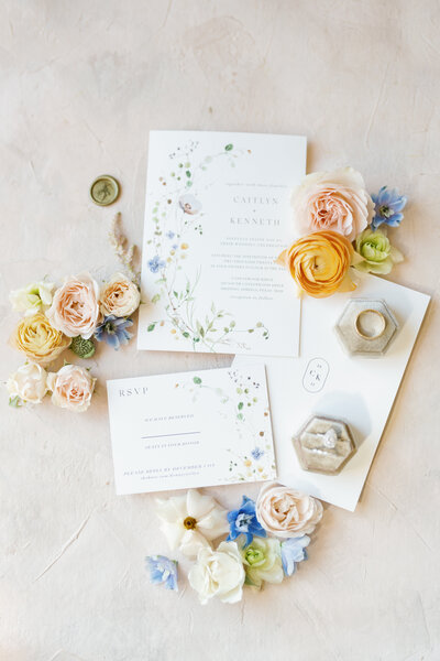 Flat lay of wedding invitation suite with wedding rings and orange flowers