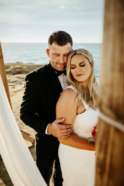 couple standing together under wooden arch during elopement at the sunset cliffs in san diego california