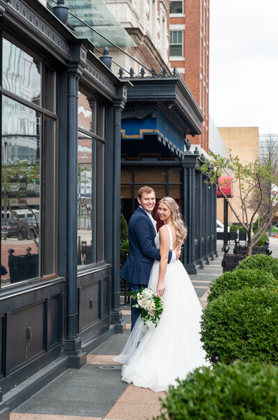 bride and groom look over their shoulders in front of the Amway Grand Plaza Hotel in downtown Grand Rapids