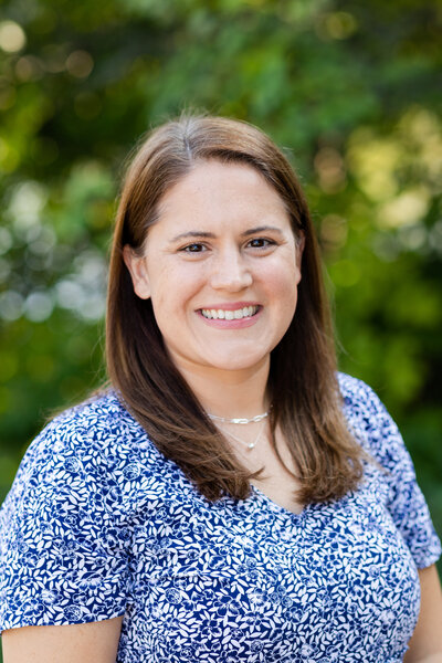 Female Professional Smiling with arms crossed casually in black blazer and cream top in front of navy brick wall at relaxed headshot photo session