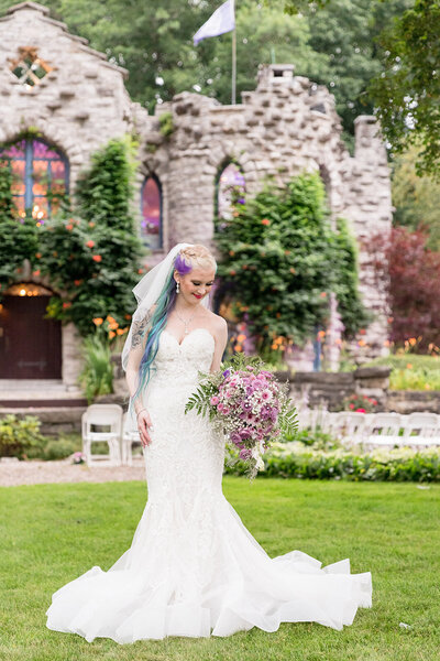 Bride by herself holding flowers looking down in front of a castle