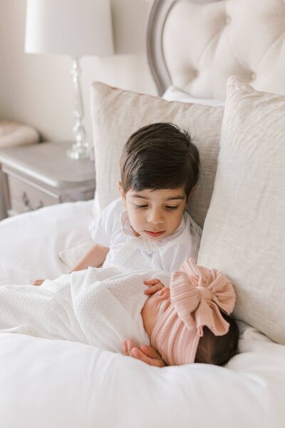 A little boy holds his baby sister on a bed during New Jersey newborn photos at home.