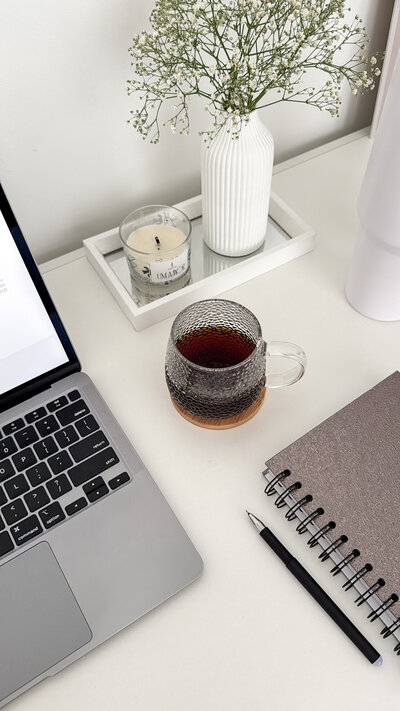 Aesthetic desk scene with a laptop, notebook, cup of tea, and candle