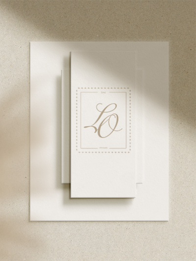 A stack of three layered ivory cards with elegant script letters “LO” and a decorative dotted border on the top card, brand design styled by Sweet Pea Ink Creative, arranged on a textured light surface.