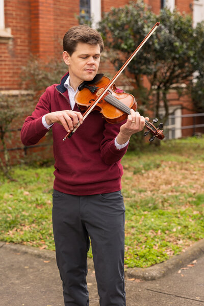 man standing in front of a church playing the violin wearing business casual outfits during brand photo session Atlanta Brand photographer