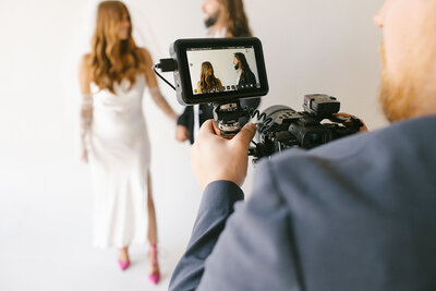 A man with a video camera records a bride taking a photo, encapsulating a memorable wedding moment.