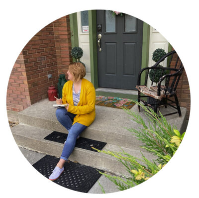 Photo is of the designer who is sitting on porch steps and looking away from the camera, while also holding a notebook and pencil.