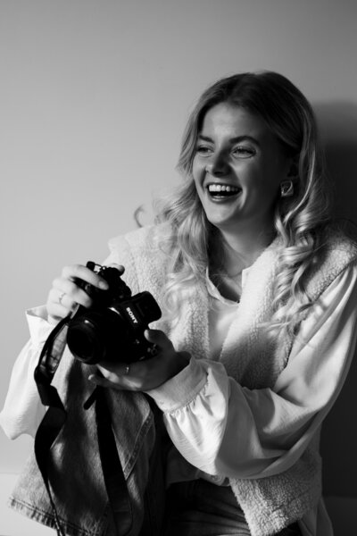 Een vrouw glimlacht terwijl ze een camera vasthoudt, klaar om mooie momenten vast te leggen.