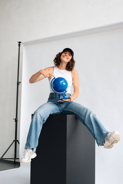 Studio Vers branding foto van vrouw met blauwe wereldbol, zittend op zwarte sokkel in een studio
