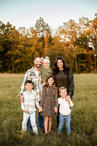 A family of six standing in the fall foliage smiling and embracing each other.