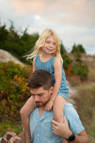 A little girl getting a ride on her dad's shoulders at Wingaersheek Beach during a family photo session.