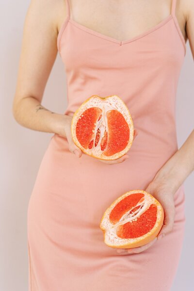Closeup of a woman wearing a pale pink strappy dress and holding 2 open grapefruit halves