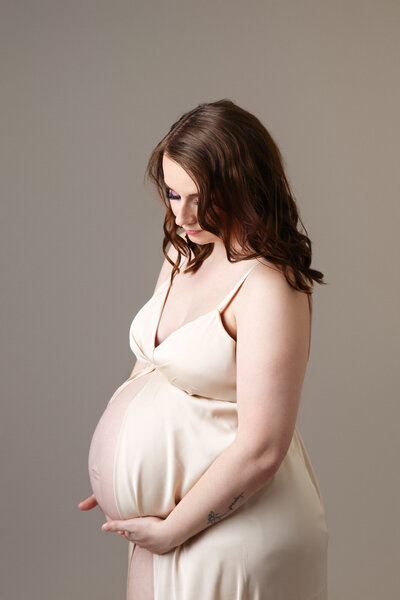 Beautiful portrait of a woman wearing a gold slip and holding her hands under her pregnant belly bump