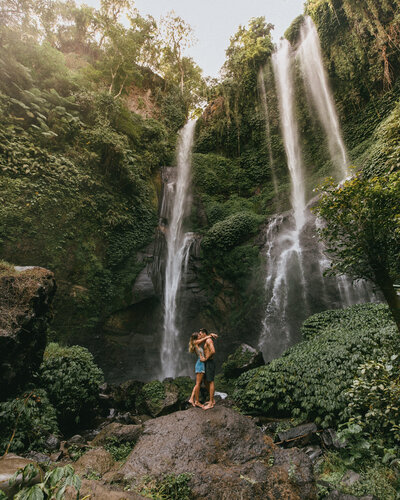 man and woman kissing in front of waterfall