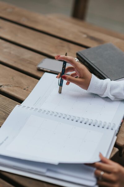 Main tenant un stylo pour écrire dans un agenda, symbolisant la prise de contact avec AE Assistante sur son agenda calendly, spécialiste des tâches administratives pour artisans et petites entreprises