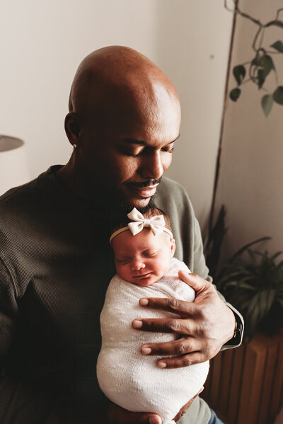 A dad holds his baby girl tight while capturing a sweet moment during their in studio newborn photo shoot in Bismarck, ND
