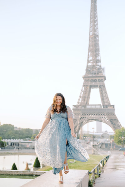 A girl in a blue dress walking in front of the Eiffel Tower in Paris. 