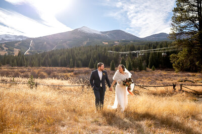 wedding couple walking hand and hand with a mountain scene behind them including a gondola overhead