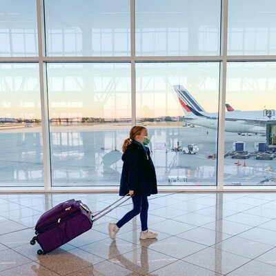 kid girl walking with her cabine bag in an airport with lanes in the background