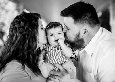 Black and white photo of family with newborn, kissing the baby