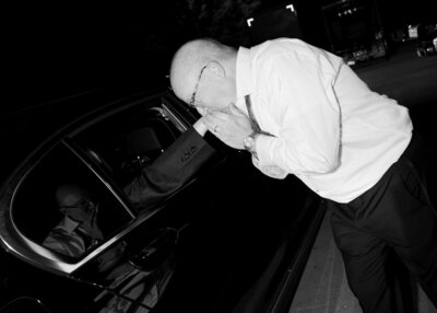 Black and white image  of dad kissing bride's hand through the window of the wedding getaway car