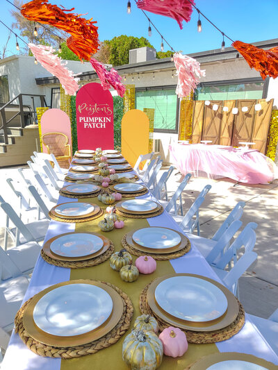 Festive outdoor pumpkin patch party table with pink and gold pumpkins, woven chargers, and colorful backdrop décor styled by Stars and Stripes Events in Arizona.