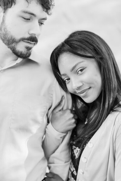 A young woman holds onto her fiance and smiles during their engagement session