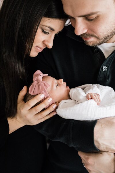 Two adults cradling and affectionately looking at a newborn baby during an at home newborn photography session.