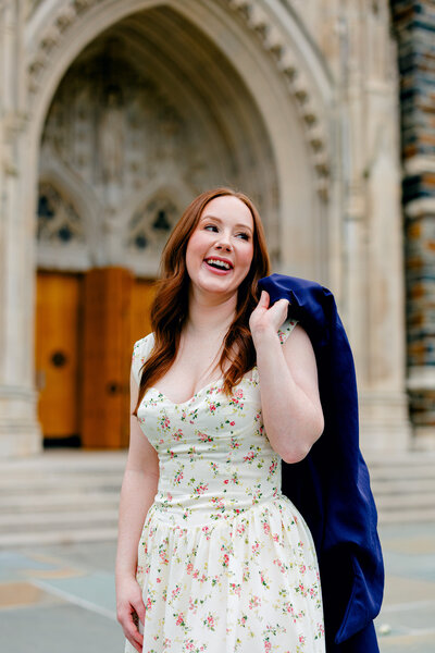 Duke University nursing graduate laughing while holding gown over her shoulder in front of Duke Chapel.