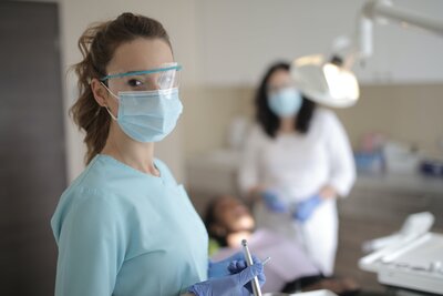A female dentist with a mask and eye protection holding dental tools.