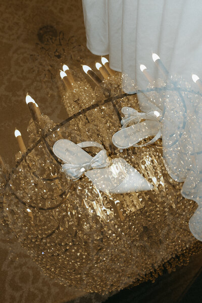 Beautiful, warm-lit chandelier with the bride’s wedding heels placed inside it