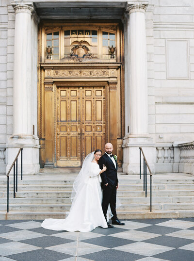 Bride and groom portrait in front of City Hall. The bride has her head on her groom's shoulder with her eyes closed. He is looking down at her.