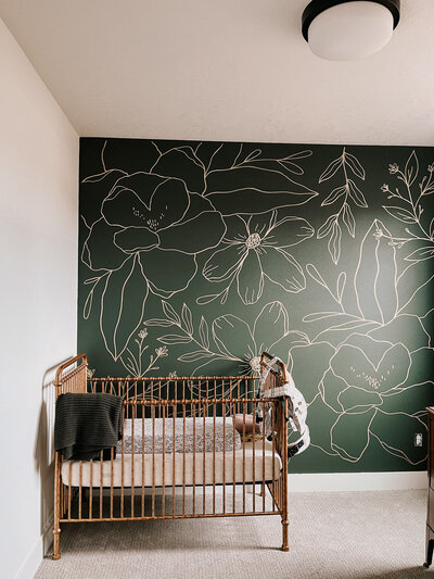 Modern floral mural on a green wall in a baby's room with a crib featuring custom calligraphy details representing full service design and calligraphy by Life in Letters.