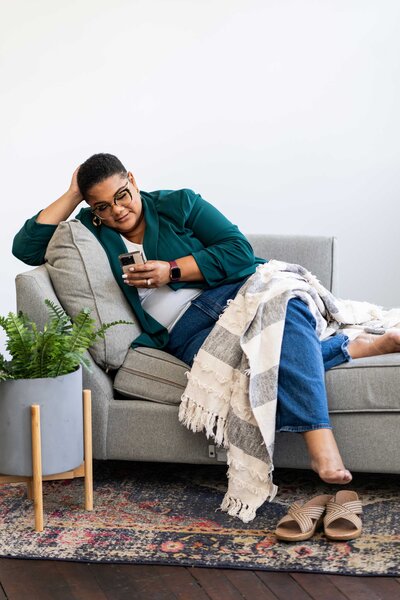 The Guided Career Pivot professional sitting on an elegant couch, dressed in a sophisticated outfit, using her phone as a tool for strategic career coaching.