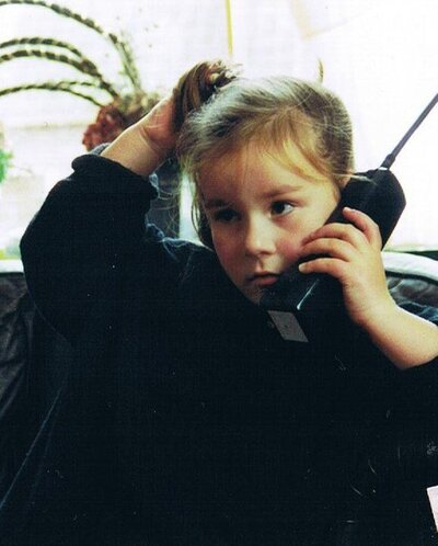 Trix in haar jongere jaren met een grote telefoon in haar hand