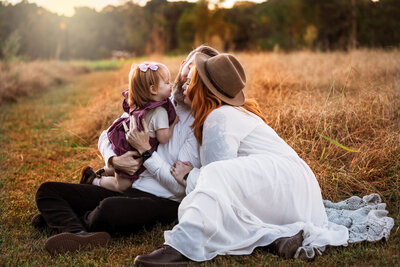 Mom and dad kidding toddler girl in a field during golden hour sunset