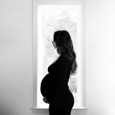 Maternity Portrait taken in Monterey County of a pregnant woman standing in front of a window.