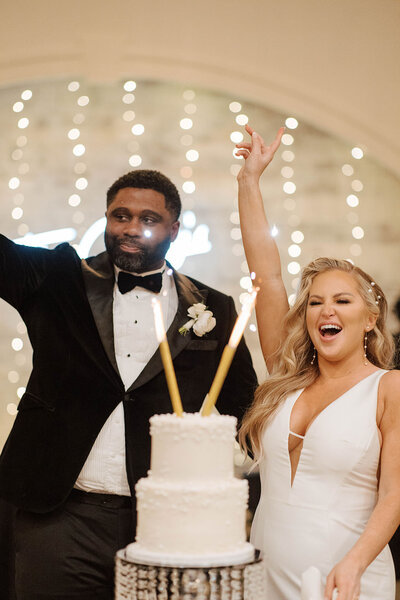 Joyful bride and groom celebrating in front of a wedding cake with lit sparklers