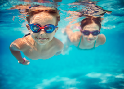 A boy, wearing goggles, happily swims underwater in the pool