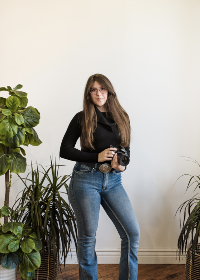 Studio branding portrait of Grace, owner of Grace LeBlanc Photography, smiling and holding her camera.