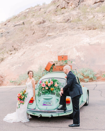 Couple poses with aqua blue volkswagen beetle getaway  car after their wedding ceremony