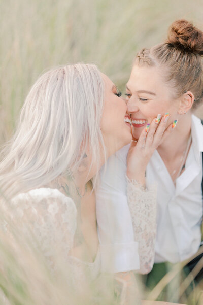 same sex couple smiling and kissing in beach grass by seattle wedding photographer, lena porter