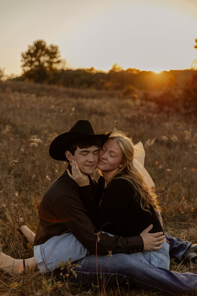 Golden hour Cowboy Engagement Photos in a Field while sitting down and holding each other 